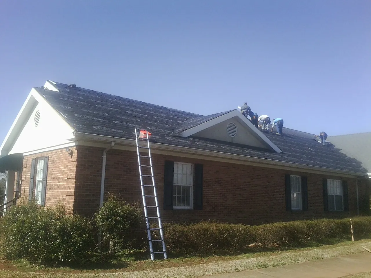 Crew tearing shingles off a brick ranch roof with a ladder set — Emergency Roof Repair work by our crew in Mc Cormick
