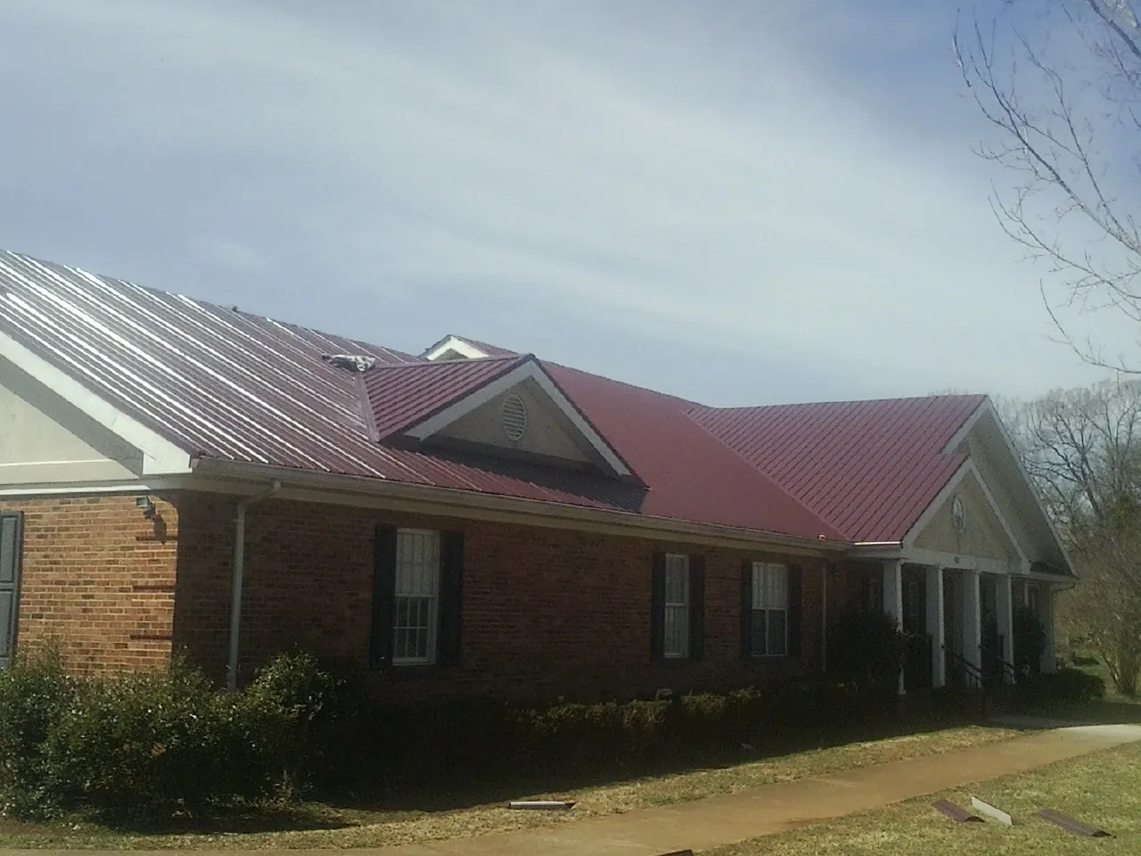 Red metal roof with gabled entries on a long brick building, from a Hail Damage Roof Repair job in Mc Cormick