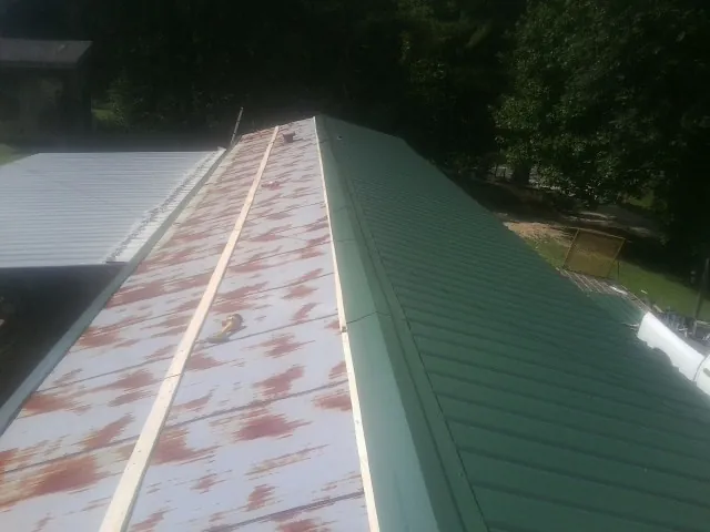 Old rusted panels beside newly installed green metal roofing — Wind Damage Roof Repair by Roofing Brothers in Mc Cormick
