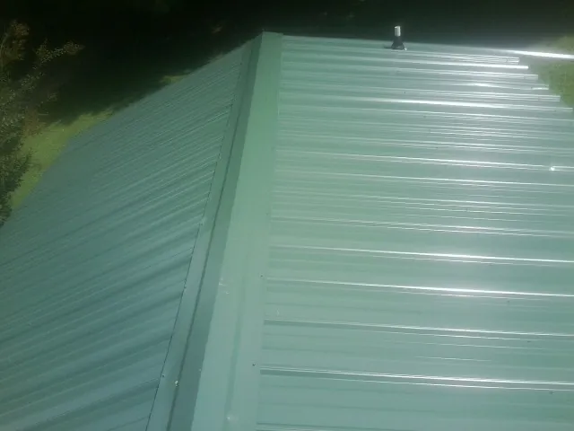 New green metal panels meeting at the ridge of a roof — Flat Roof Repair work by our crew in Mc Cormick