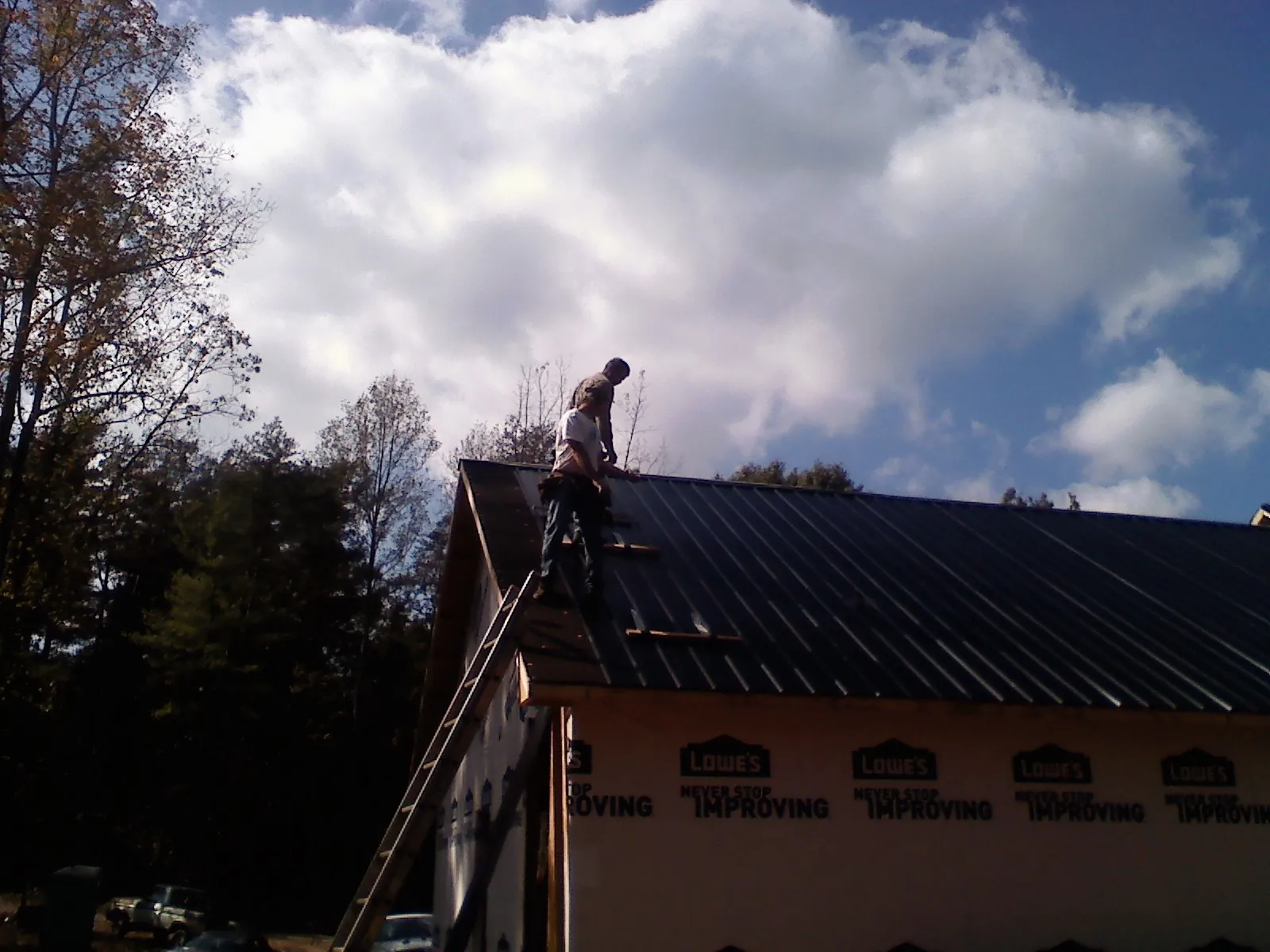 Roofer fastening dark metal panels high against a cloudy sky, from a Roof Inspection job in Mc Cormick