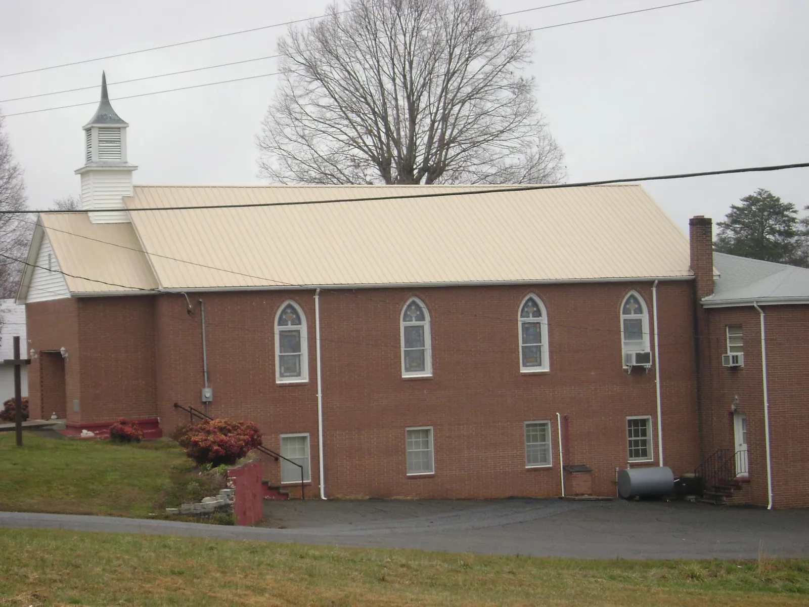 New tan metal roof on a brick church with a white steeple in Mc Cormick